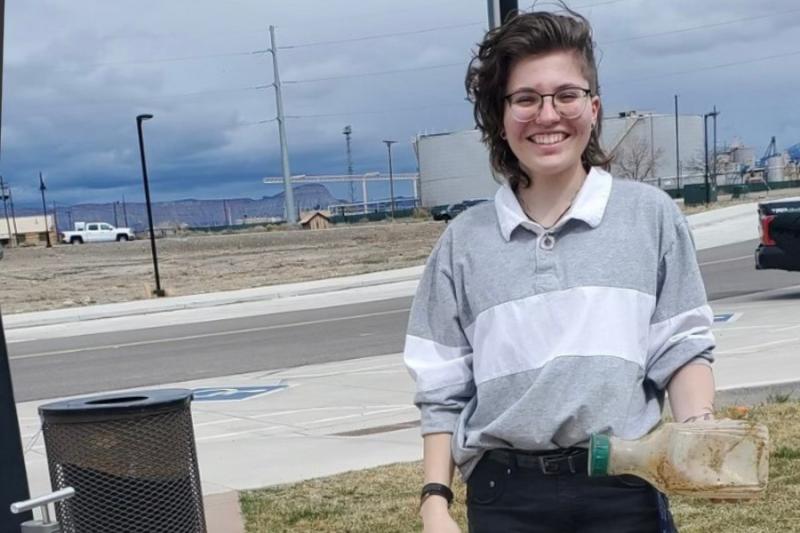 Woman holding piece of trash near black trash bin.