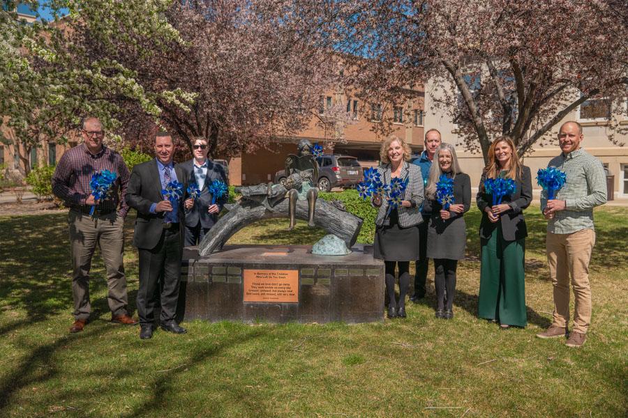 County officials stand next to statue of child holding blue pinwheels. 
