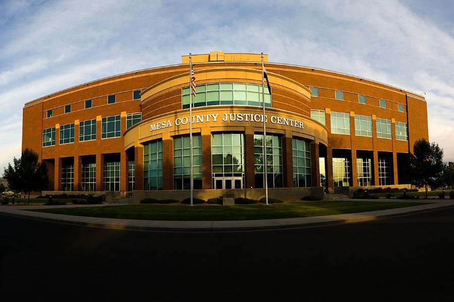 Brick building with white sign reading, "Mesa County Justice Center," with American flag and Colorado flag outside. 