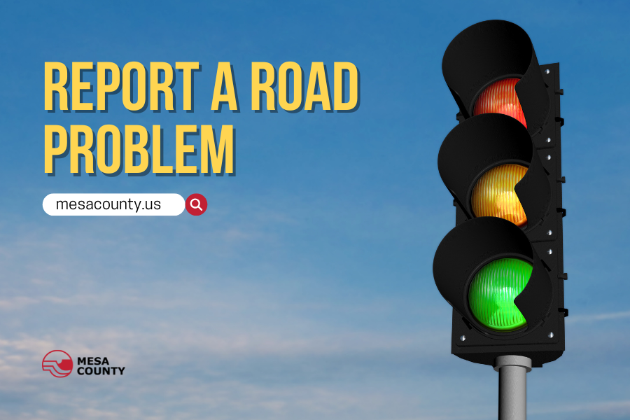 Red, yellow, and green traffic light with yellow text reading, "REPORT A ROAD PROBLEM mesacounty.us," and the red and black Mesa County logo.