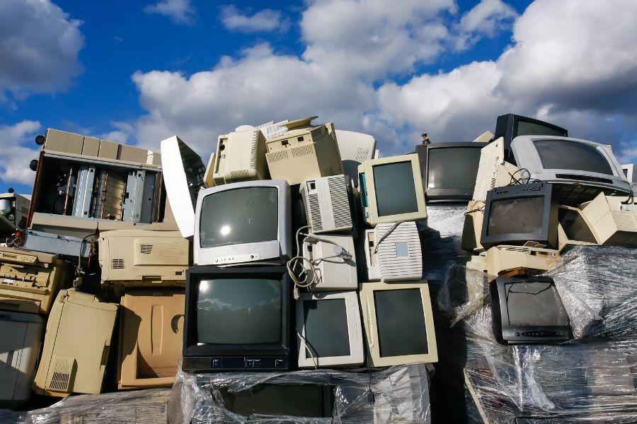 Stack of old TVs and electronics on front of blue sky with white clouds.