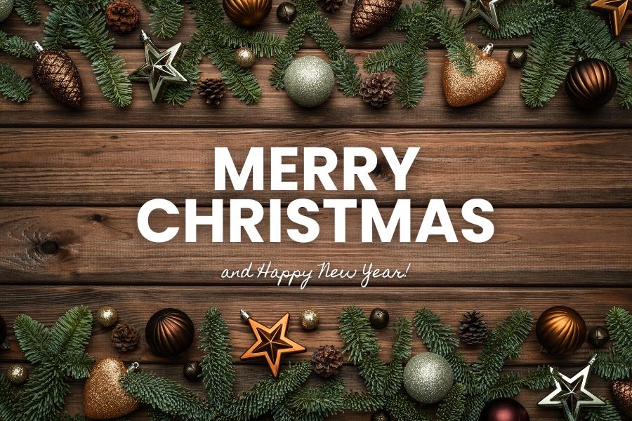Dark wood with green pine tree cuttings, pine cones, and shiny ornaments on the top and bottom with white text reading, "Merry Christmas and Happy New Year!"