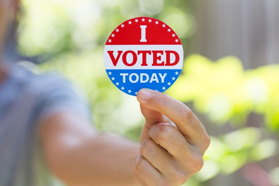 Blurry girl holding clear red, white and blue sticker reading, "I VOTED TODAY."