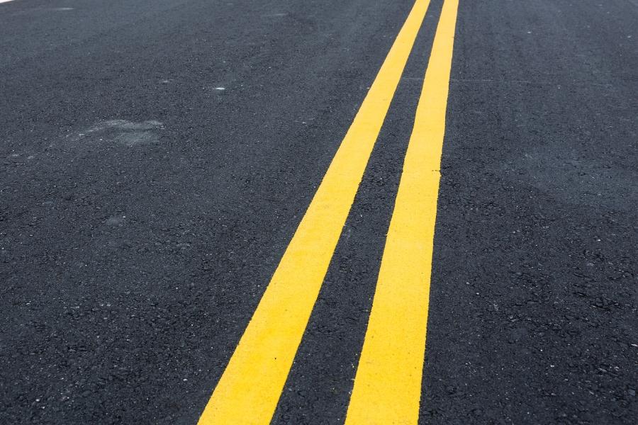 Black paved road with double yellow lines painted down the middle. 