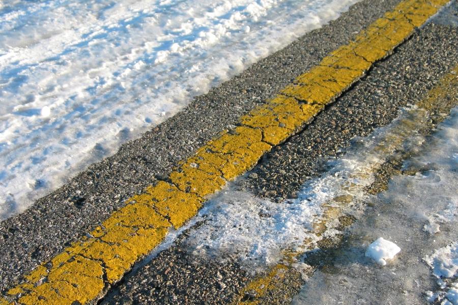 Semi-icy road with double yellow lines peaking through the ice and snow. 
