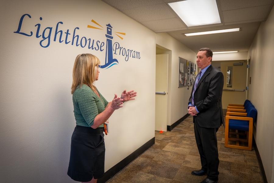 A woman speaking to a man in a hallway with a blue and yellow Lighthouse Program logo on the wall. 