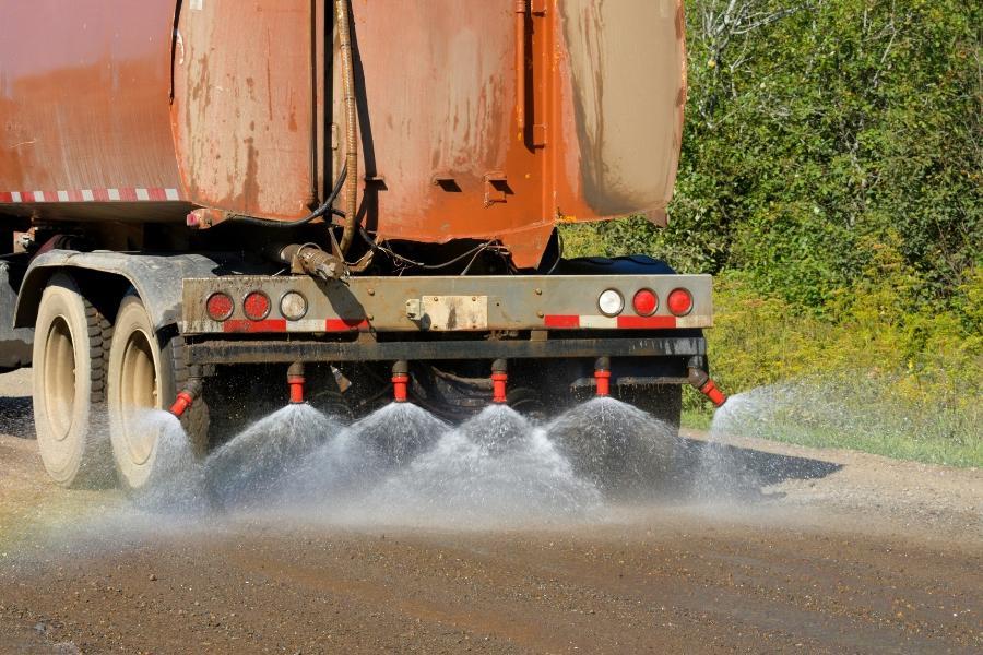 The back of a brunt orange truck spraying liquid out of six compartments. 