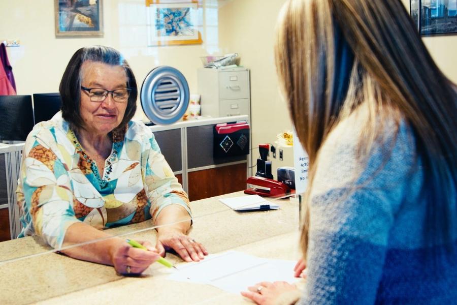 A woman points to a paper with a pen at a customer service window. 