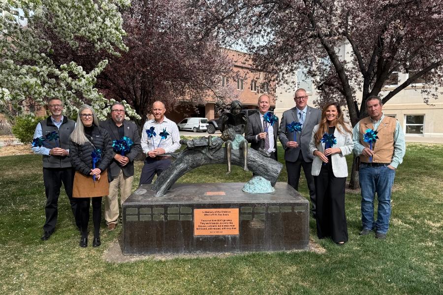 A group of people holding blue pinwheels, standing by a statue of a child. 
