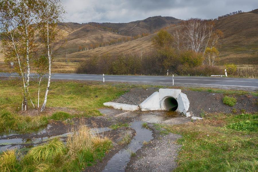 A concrete culvert under a road with water coming out. 