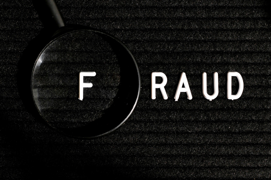 Fraud spelt in letters on a black background with a magnifying glass.