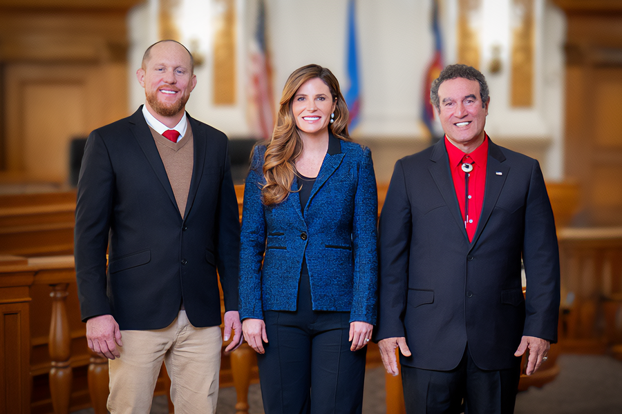 One woman is standing in the middle of two men (Board of Mesa County Commissioners), smiling in professional clothing. 