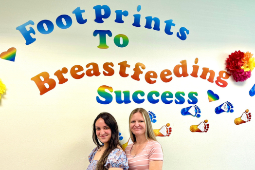 two women in front of colorful sign with text 'footprints to breastfeeding success'