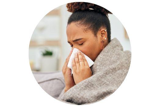 a person wrapped in a gray wool blanket is blowing their nose into a white tissue while sitting on a couch.