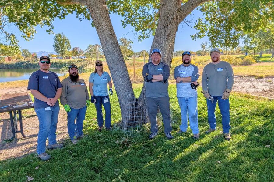 Six people standing by a tree smiling. 