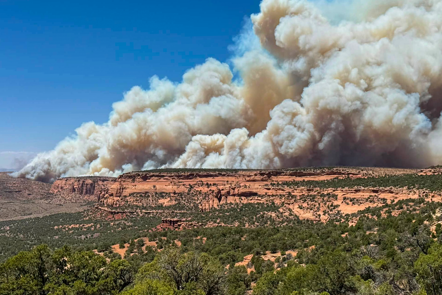 A helicopter drops water on the Snyder Fire as smoke rises from burning vegetation in rugged terrain near the Utah-Colorado border.